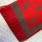 A close-up of a red and grey woven scarf with a deer pattern and fringed edge, laid on a white patterned surface.