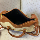A tan and cream canvas handbag with gold-tone hardware, shown open to display its black interior. The bag features double top handles and a shoulder strap.