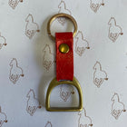 A horse-themed keychain featuring a red leather strap with a gold snap button, attached to a gold-tone metal D-ring and key ring, displayed on a white background with a repeating brown horse outline pattern.
