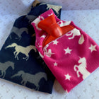 Pink and white unicorn hot water bottle cover with red bottle, sitting with a blue horsey print cover