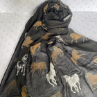 A dark gray scarf with an allover horse print in tan, white, and black, draped in a loose fold against a patterned white background.