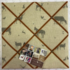 A fabric-covered pinboard with a beige linen-likefabric with country animal print, framed by brown velvet ribbon diagonals. A small product tag is attached near the lower center, and the board is photographed from above on a patterned white surface.