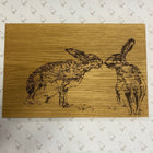 Wooden board with engraved image of two hares on a patterned background