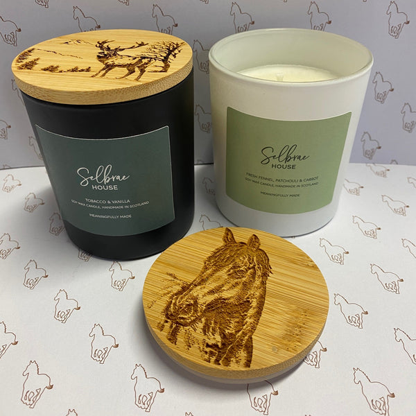 Two candles with wooden lids featuring animal engravings on a patterned background.