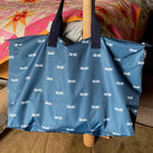 A navy overnight bag with an all over white dragonfly print by Sophie Allport, hanging on a bed post.