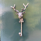 A rustic metal deer head hook with antlers mounted on a dark green painted wooden door.