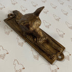 A bronze-finished metal door knockershaped like a fox head on a rectangular base, photographed on a white background with a repeating brown horse outline pattern.