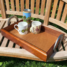 Wooden tray with mugs and horseshoe handle on a wooden bench outdoors.