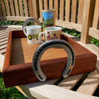Wooden tray with mugs, horseshoe handles on a wooden bench outdoors.