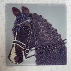 A square glass or acrylic art panel featuring a stylized horse head crafted from purple and dark gray beads, with white bead accents on the bridle and nose. The panel is photographed from above on a white patterned surface.