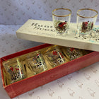 A vintage set of six Hunter Scenic glassware shot glasses, shown in their original red and cream-colored presentation boxes. The shot glasses feature a scenic winter mountain landscape illustration with red snow and gold borders.