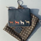 A small navy leather coin purse with zip top opening. Four coloured horses stitched onto the front. Shown on a Mala Leather flower printed pouch.