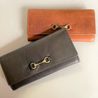 Two leather purses, one in tan brown and one in black, both with brass snaffle detail on the front.